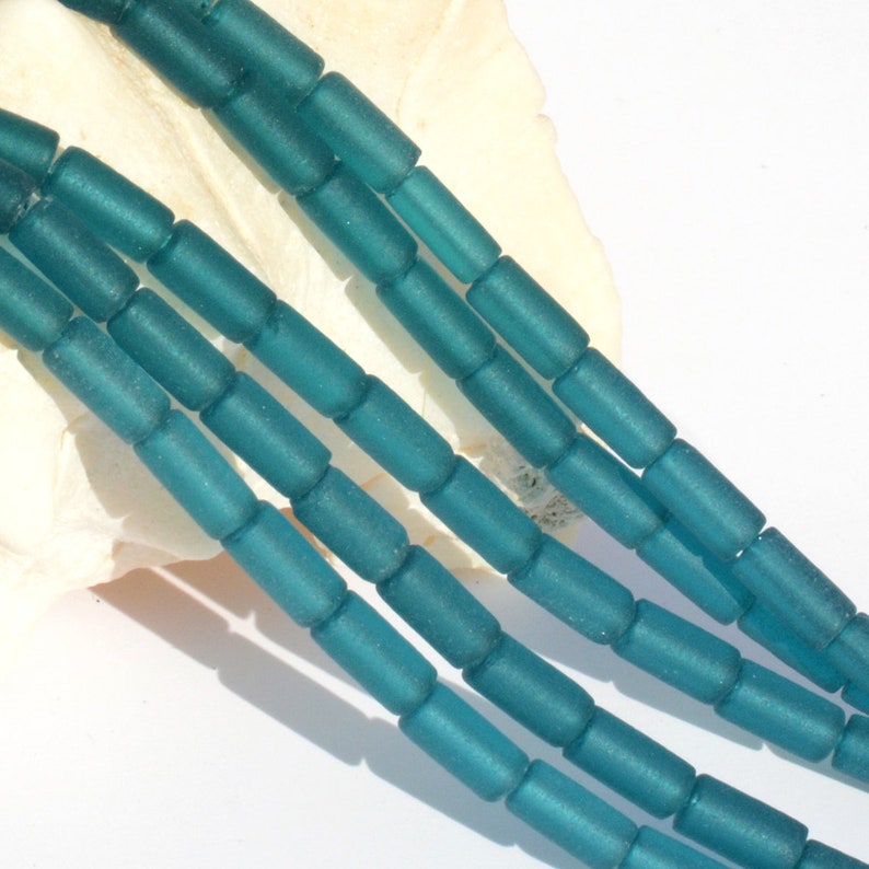 May include: Teal blue glass beads, frosted and cylindrical in shape. The beads are strung together in a long strand.