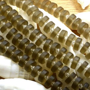 May include: A strand of dark brown glass beads with a faceted, donut-shaped design. The beads are strung on a clear thread.