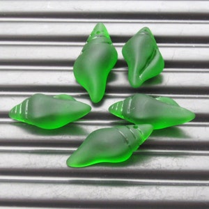 May include: Five green glass seashells in the shape of a conch shell. The shells are frosted and have a smooth, polished finish.