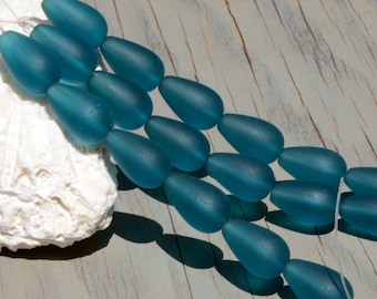 May include: A strand of teal blue glass beads in a teardrop shape. The beads are frosted and have a matte finish.
