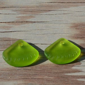 May include: Two lime green glass pendants with a hole at the top and a textured design around the edge.
