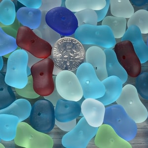 May include: A collection of smooth, colorful glass beads with a hole in the center. The beads are in shades of blue, green, red, and white. A US dime is included for scale.
