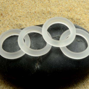 Puede incluir: Cuatro anillos de vidrio esmerilado apilados sobre una piedra negra. Los anillos son translúcidos y tienen un acabado liso y pulido.