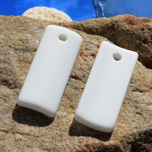 May include: Two white rectangular ceramic pendants with a hole at the top for hanging. The pendants are smooth and have rounded edges.