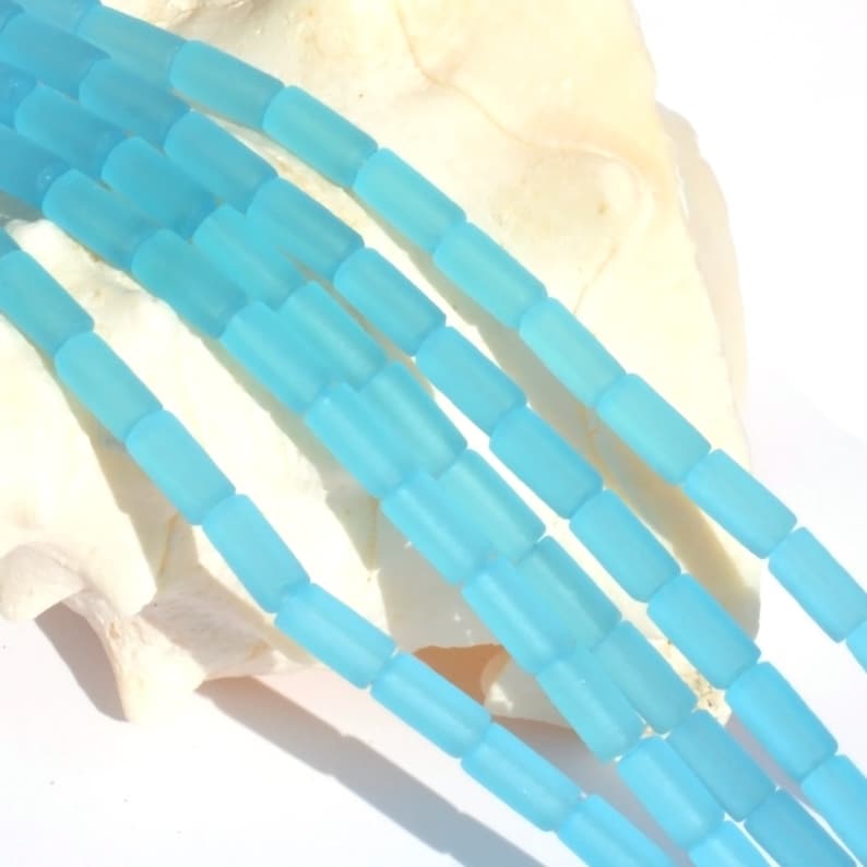 May include: A strand of light blue frosted glass beads. The beads are rectangular in shape and have a matte finish.