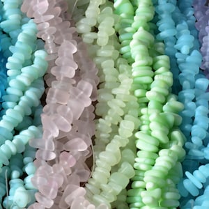 May include: Assortment of colorful sea glass beads in shades of blue, green, and purple. The beads are strung together in strands and are perfect for jewelry making.