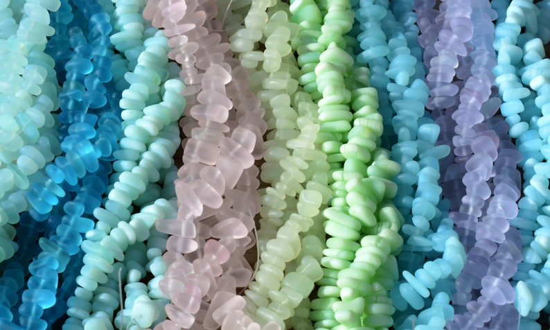 May include: Assortment of colorful sea glass beads in shades of blue, green, and purple. The beads are strung together in strands and are perfect for jewelry making.