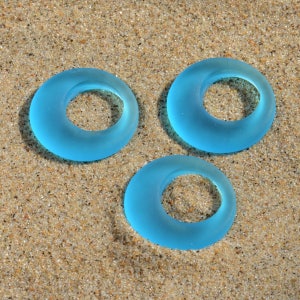 May include: Three light blue glass rings on a sandy surface. The rings are smooth and have a frosted finish.