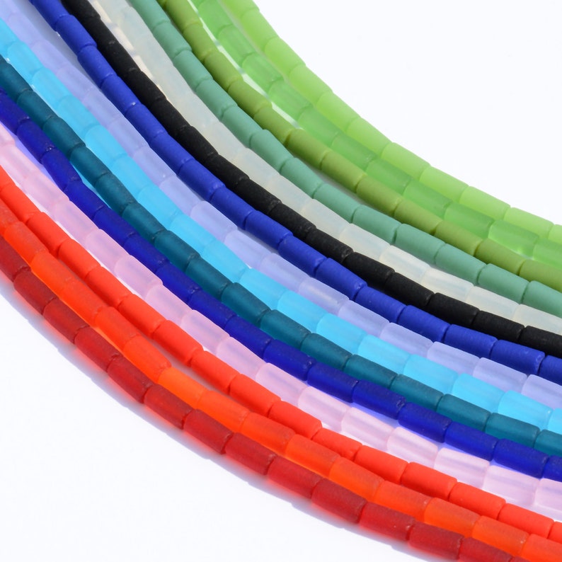 May include: A rainbow assortment of glass beads, each strand a different color, including red, orange, yellow, green, blue, purple, and white. The beads are all the same size and shape, and they are arranged in a fan shape.
