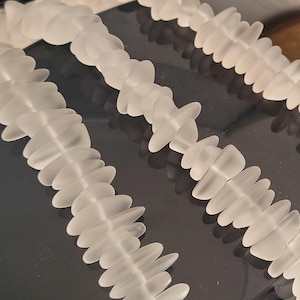 May include: Three strands of frosted glass beads, each strand is made of small, flat, oval-shaped beads. The beads are arranged in a staggered pattern, creating a textured look.