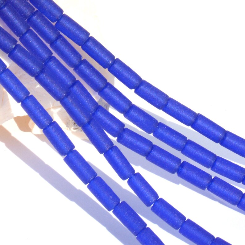 May include: A strand of blue glass beads, each bead is a cylinder shape with a frosted finish.