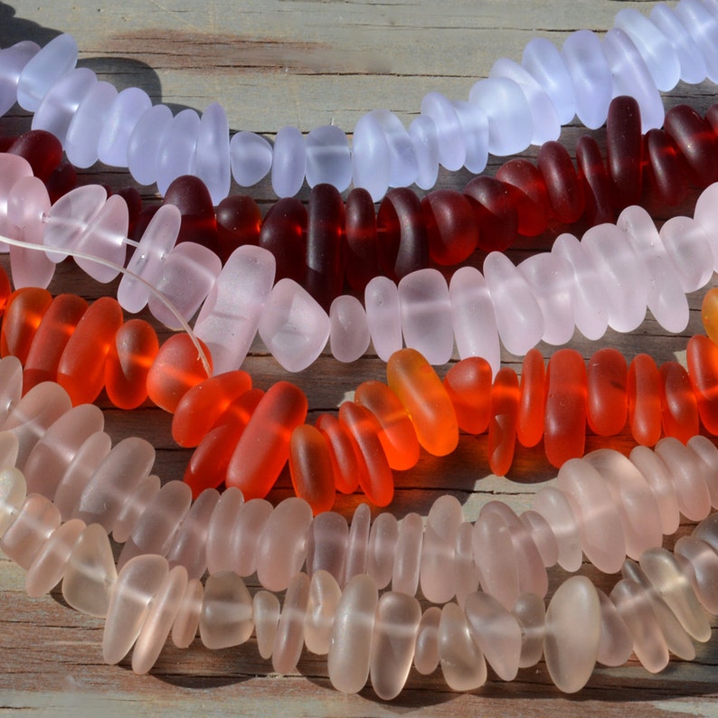 May include: A collection of colorful glass beads in various shades of pink, red, and blue. The beads are arranged in rows, with the lightest color at the top and the darkest color at the bottom. The beads are all smooth and have a slightly frosted finish.