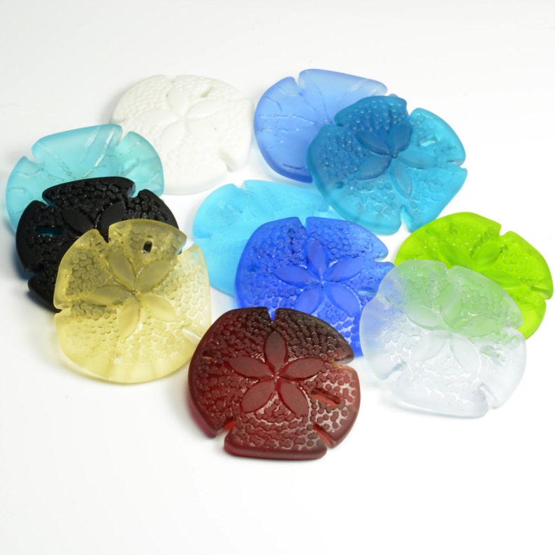 Pu&ograve; includere: Assortimento di ornamenti di dollari di sabbia di vetro colorati in varie tonalit&agrave; di blu, verde, rosso, bianco e nero. I dollari di sabbia sono tutti di dimensioni approssimativamente uguali e hanno un design rialzato e testurizzato.