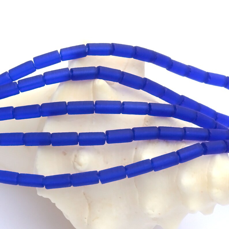 May include: A strand of blue glass beads, each bead is a rectangular shape with a frosted finish.