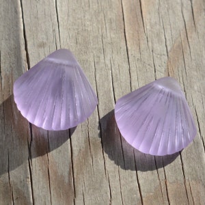 Puede incluir: Dos conchas de vidrio púrpura con textura acanalada. Las conchas están sobre una superficie de madera.