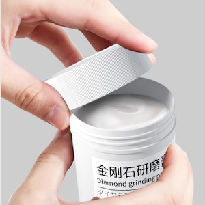 May include: A white container with a screw-on lid is being opened, revealing a creamy substance inside. The container has text in Japanese and English that reads "Diamond grinding paste."