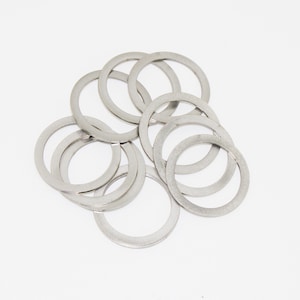 Puede incluir: Un conjunto de arandelas circulares de color plateado sobre un fondo blanco. Las arandelas tienen forma de anillo con un ancho uniforme. El metal presenta un acabado mate, reflejando una luz suave. Cada arandela mide unos 2,5 cm de diámetro.