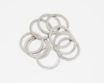 May include: A collection of silver-colored, circular washers arranged on a white background. The washers have a flat, ring-like shape with a consistent width. The metal appears to have a matte finish, reflecting soft light.