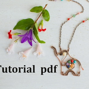 May include: A copper wire elephant necklace with colourful gemstone accents. The necklace is on a white wooden surface with a sprig of flowers.