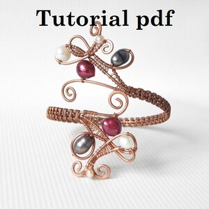 May include: A copper wire bracelet with a woven band and intricate wire designs. The bracelet is adorned with white, grey, and burgundy beads.