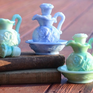 Puede incluir: Tres botellas de perfume vintage de vidrio con diseños de rosas. Las botellas son de color azul y verde y están colocadas sobre dos libros antiguos.