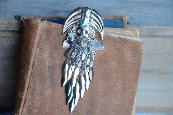 A chunky avant-garde mermaid brooch assembled from creepy doll parts — wearable assemblage art that belongs in a gallery.