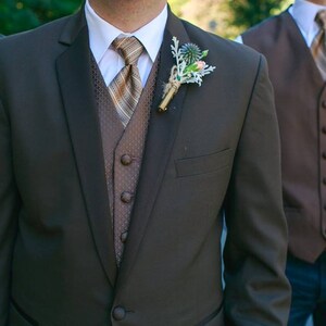 May include: A brown suit jacket with a brown vest and a striped tie. The suit jacket has a boutonniere with a small flower.