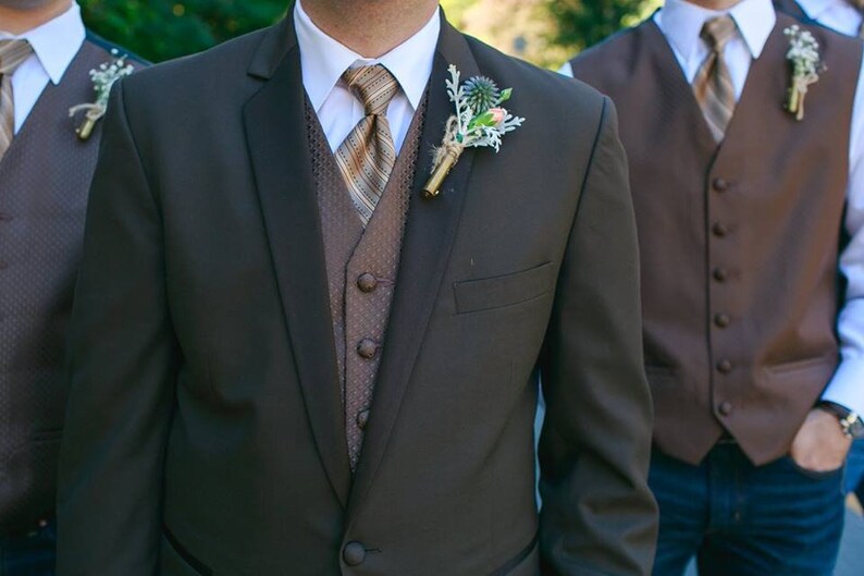 May include: A brown suit jacket with a brown vest and a striped tie. The suit jacket has a boutonniere with a small flower.
