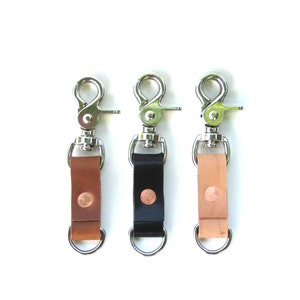 May include: Three leather keychains with metal clasps and rings. The keychains are brown, black, and tan.