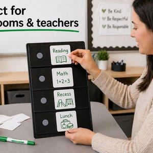 May include: A black classroom schedule board with white labels for Reading, Math, Recess, and Lunch. A person is placing a label on the board. The board is on a table with a green marker and a stack of blank labels.