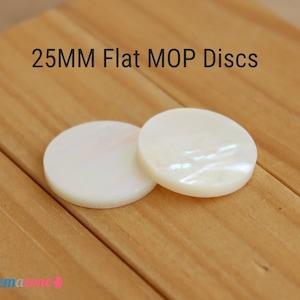 May include: Two 25mm flat MOP discs with a pearlescent sheen, resting on a light brown wooden surface. The discs are round and have a smooth, polished appearance. Text on the image reads "25MM Flat MOP Discs."