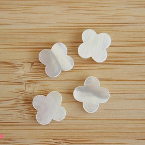 May include: Four white mother of pearl flower-shaped embellishments on a wooden surface.