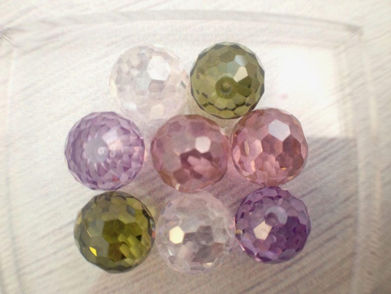 May include: A collection of eight faceted glass beads in various shades of purple, pink, and green. The beads are round and have a shiny, iridescent finish.