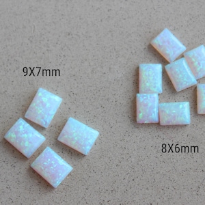 May include: Several rectangular, iridescent opal gemstones in two sizes: 9x7mm and 8x6mm. The opals have a milky white base color with flashes of blue, green, and pink. They are arranged on a neutral, textured surface.