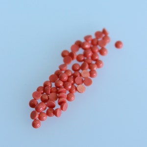 Peut inclure: Une dispersion de petites perles rondes de couleur corail sur une surface bleu clair.