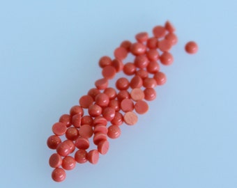 May include: A scattering of small, round, coral-colored beads on a light blue surface.