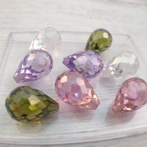 May include: Assortment of teardrop-shaped crystal beads in various colors, including clear, purple, pink, and green. The beads are faceted and have a pearlescent finish.