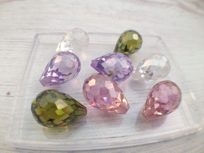 May include: Assortment of teardrop-shaped crystal beads in various colors, including clear, purple, pink, and green. The beads are faceted and have a pearlescent finish.