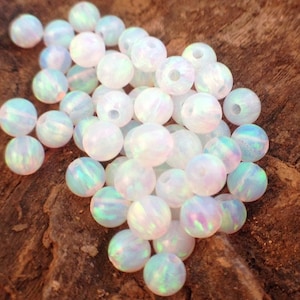 May include: A pile of white opal beads with iridescent rainbow colors. The beads are round and smooth, and they are perfect for jewelry making.