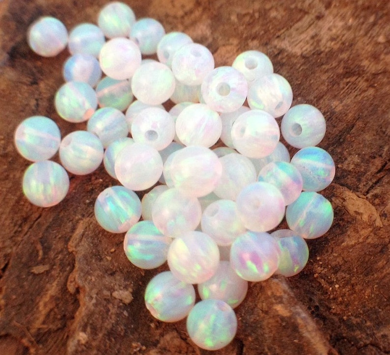 May include: A pile of white opal beads with iridescent rainbow colors. The beads are round and smooth, and they are perfect for jewelry making.