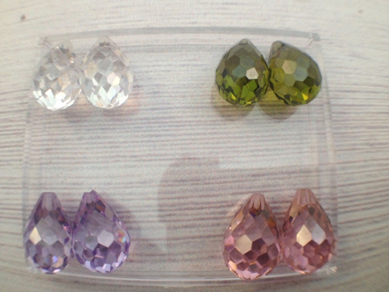 May include: Six teardrop-shaped crystal beads in a clear plastic container. Two beads are clear, two are green, and two are purple.