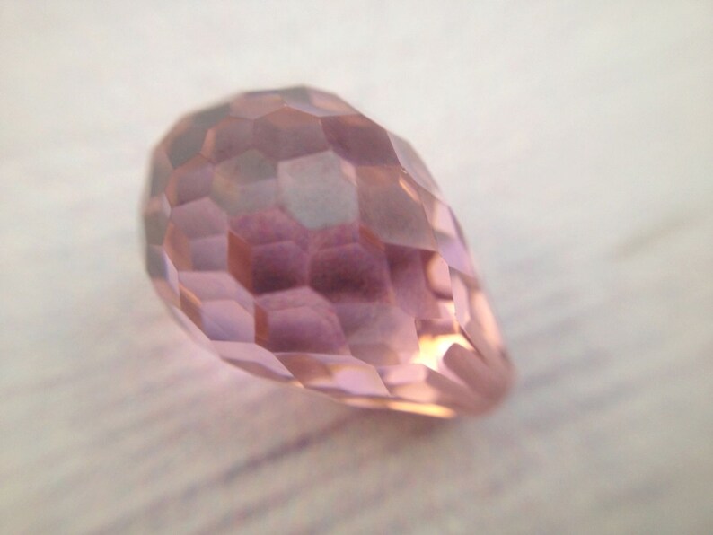 May include: A faceted, teardrop-shaped crystal bead in a pale pink color.