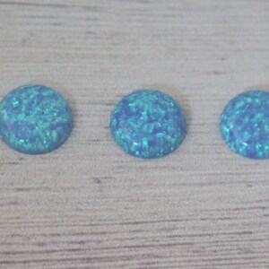 May include: Three round, light blue opal cabochons with a green iridescent shimmer.