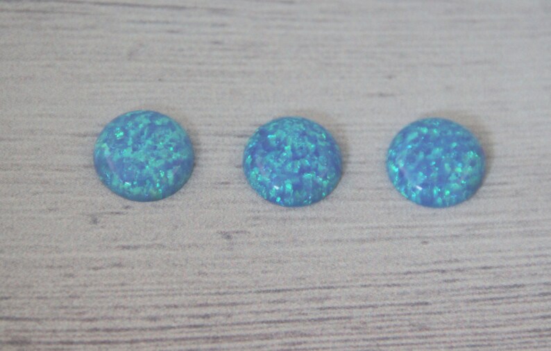 May include: Three round, light blue opal cabochons with a green iridescent shimmer.