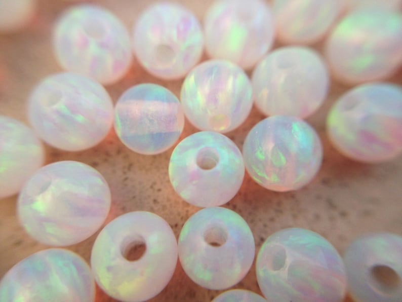 May include: A collection of white opal beads with iridescent rainbow colors. The beads are round and have a smooth, polished finish.