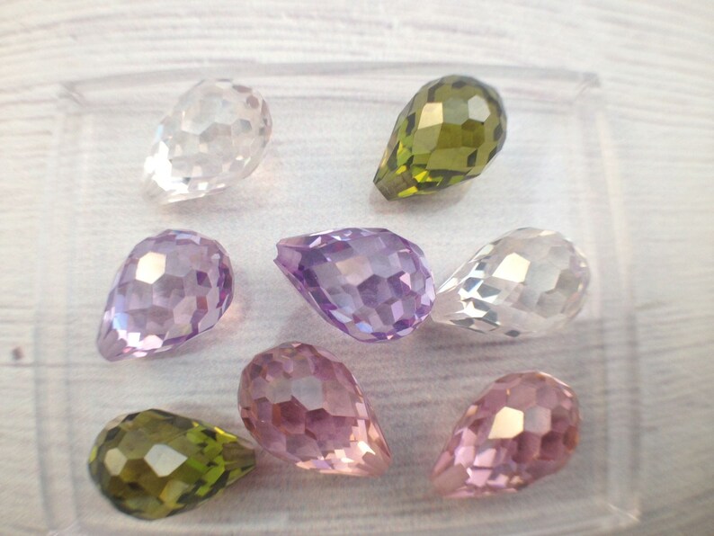 May include: Assortment of eight faceted teardrop-shaped glass beads in various colors, including clear, purple, pink, and green.