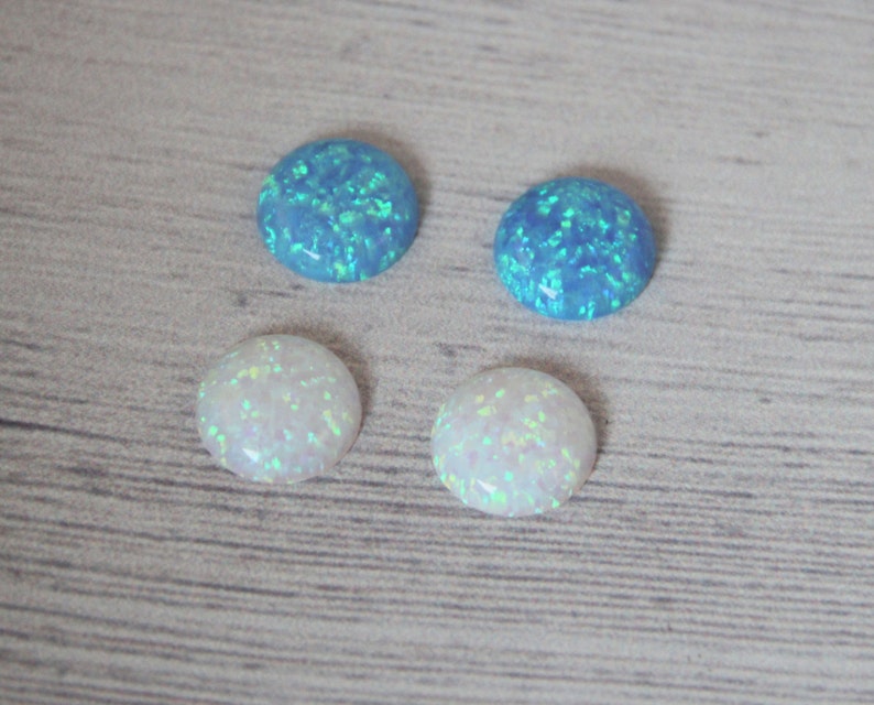 May include: Four round opal cabochons, two are white and two are blue. The opals have a sparkly, iridescent finish.