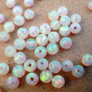 May include: A collection of white opal beads with iridescent rainbow colors. The beads are round and have a smooth, polished finish.