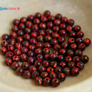 May include: A bowl filled with approximately 100 small, round, red and black iridescent beads. The beads have a shiny, reflective surface.