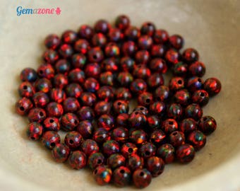 May include: A bowl filled with approximately 100 small, round, red and black iridescent beads. The beads have a shiny, reflective surface.